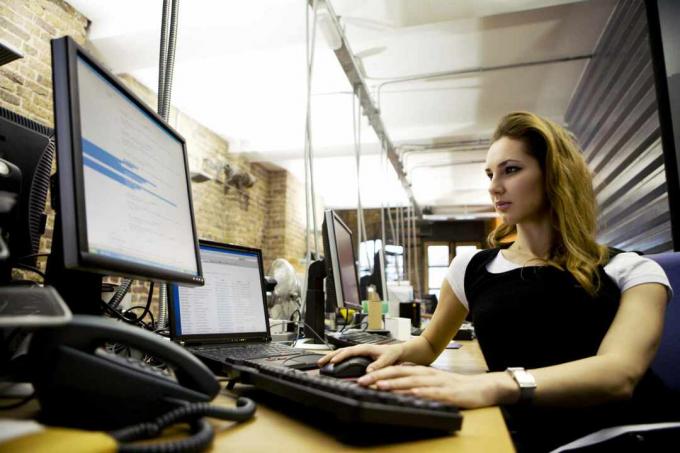 Žena koja sjedi za stolom uz prijenosno računalo s vanjskom tipkovnicom i monitorom.