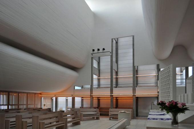 minimalistički namještaj ispod golemog, zakrivljenog stropa s bijelim naborima betona ispod klesarskih prozora