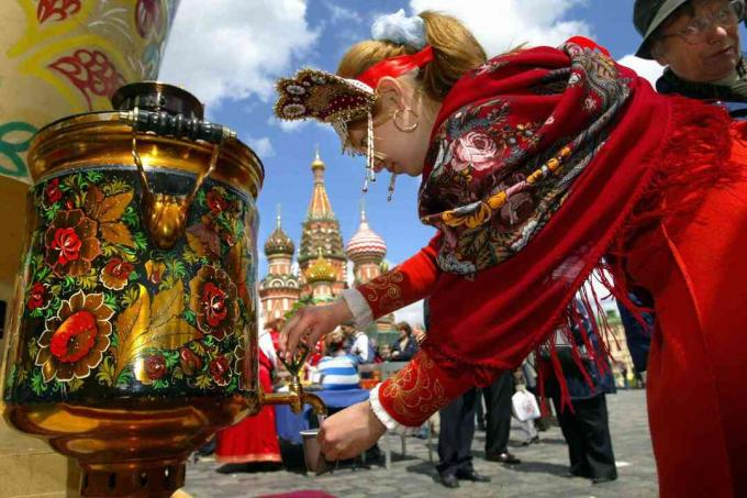 Ruska djevojka u tradicionalnoj odjeći izliva vodu iz samovara
