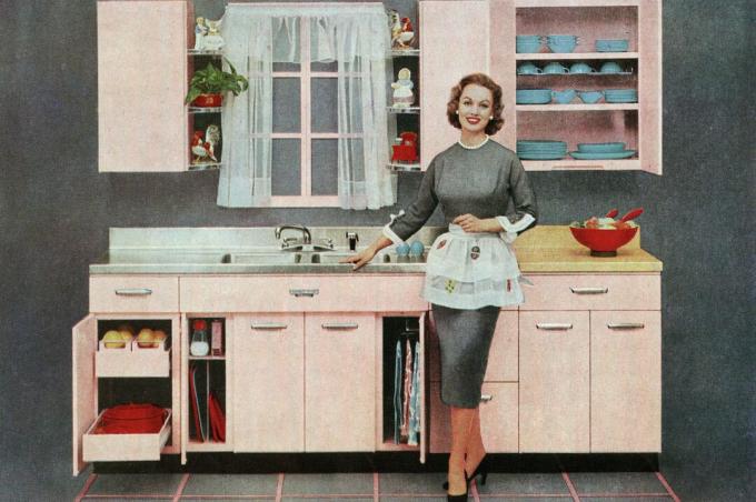 Vintage ilustracija moderne domaćice koja stoji ispred svoje nove ružičaste kuhinje, 1957