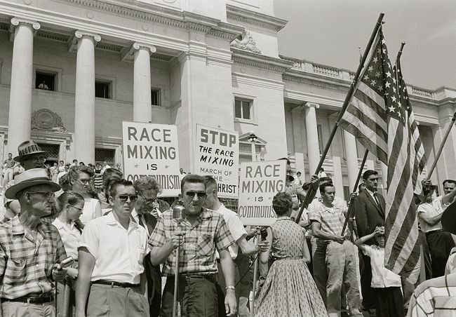 Ljudi koji drže natpise i američke zastave koji prosvjeduju zbog upisa " Little Rock Nine" u Srednju srednju školu.